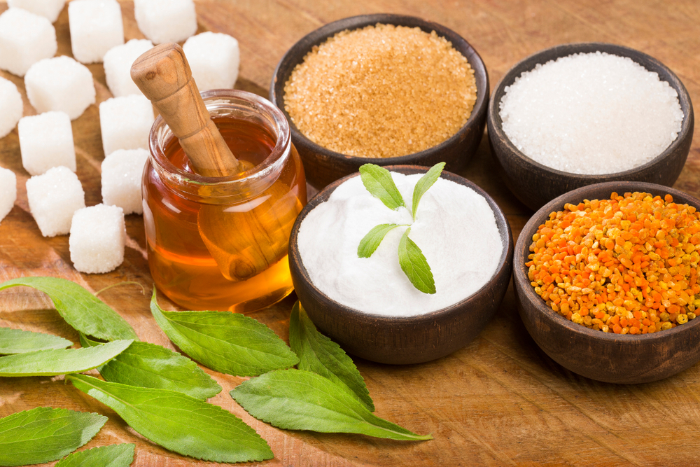 Various natural sweeteners on a table including honey, maple syrup, and stevia